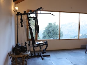 A gym with exercise equipment, a window with a view of trees, and a wicker basket with weights. - Hidden Trails Ramgarh (Ramgarh)