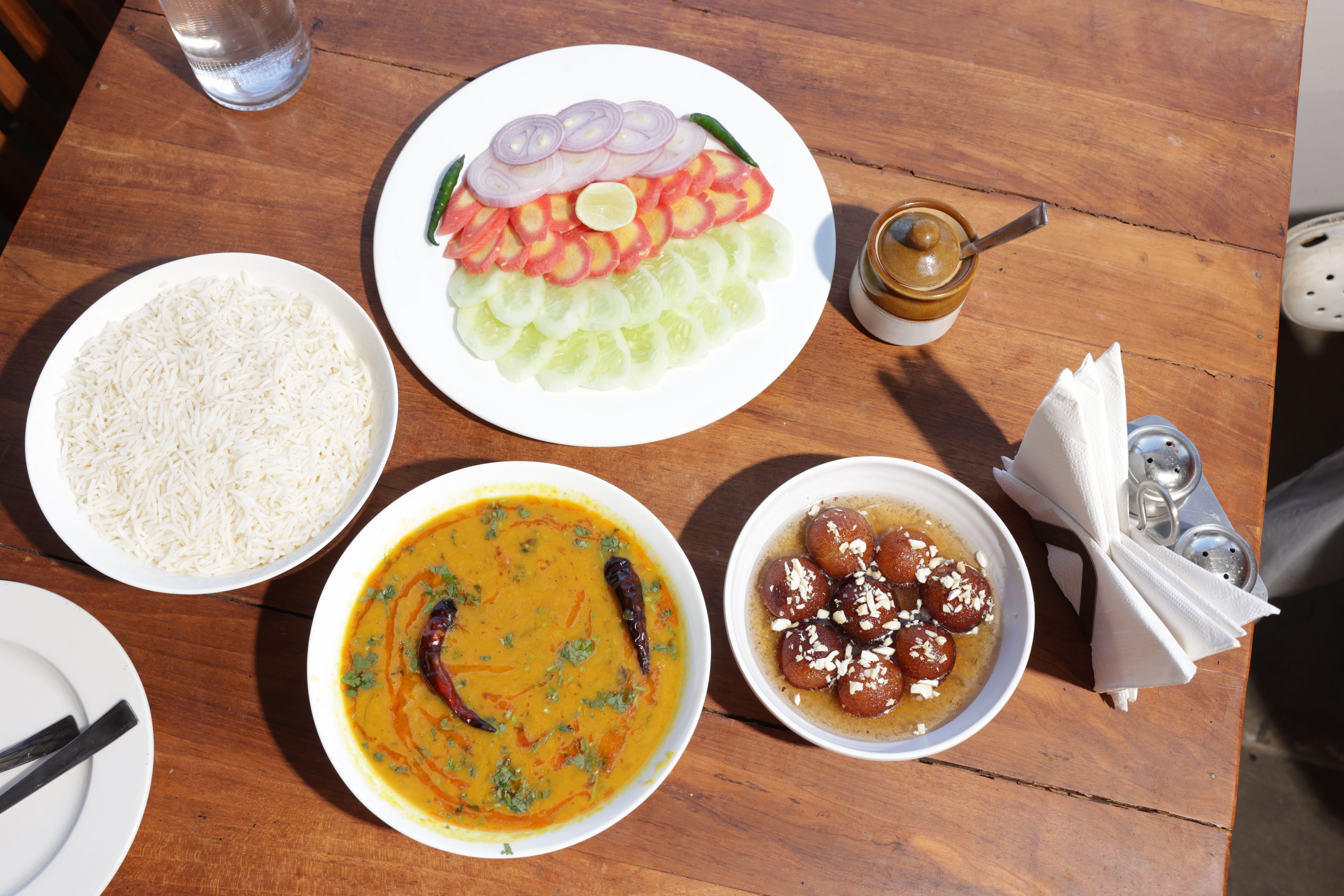 A wooden table with various dishes including rice, a curry, and sweets.