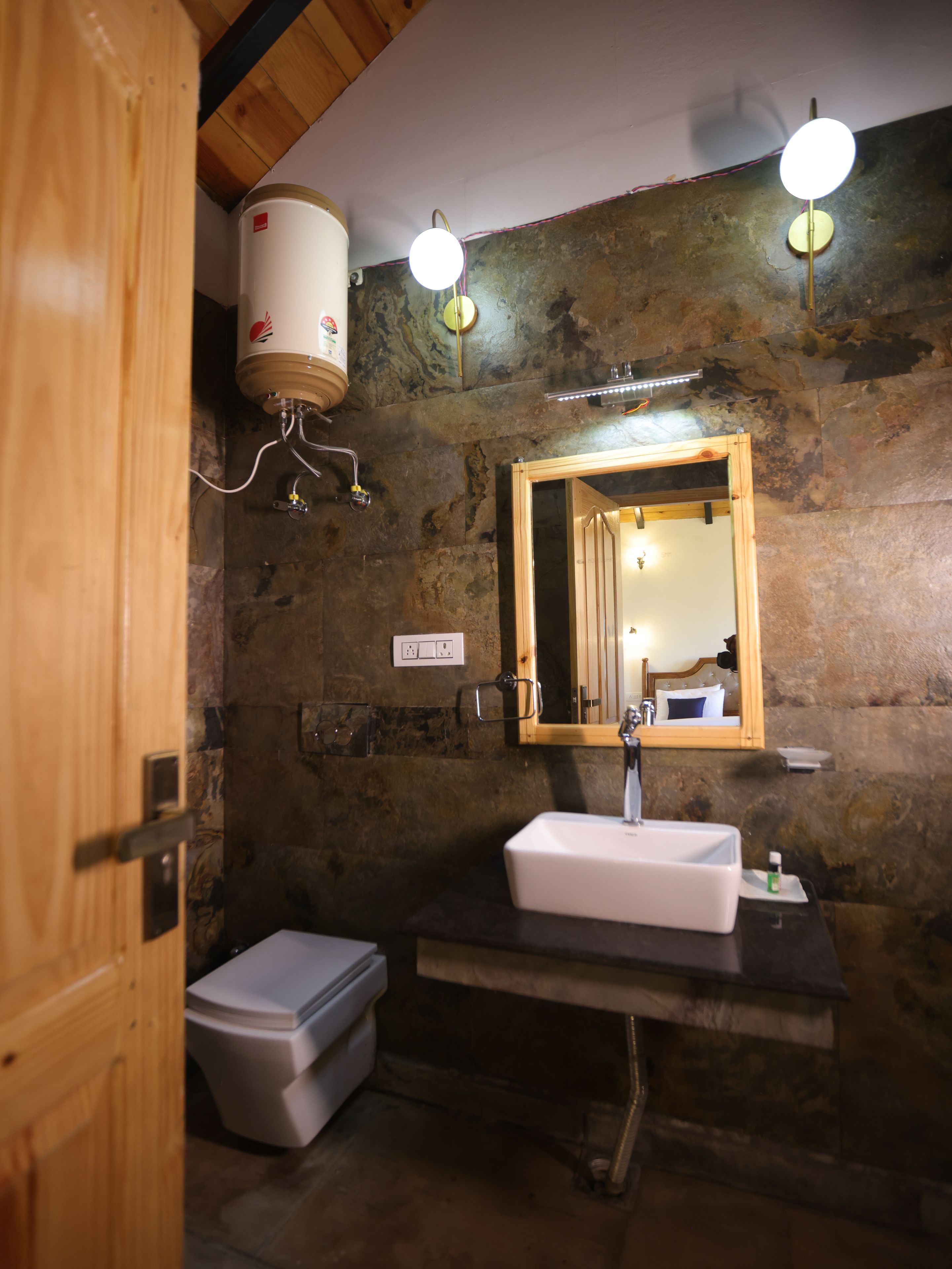 Ein Badezimmer mit einer Steinsäule, einer Holztür, einem weißen Waschbecken, einem Spiegel und einer Toilette.