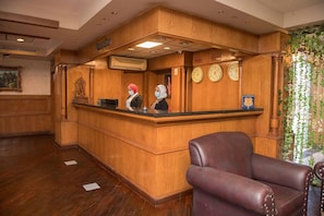 A reception desk with a wooden finish, a clock, and a chair in a lobby area. - Cecil Hotel - Ras Sedr (Ras Sudr)