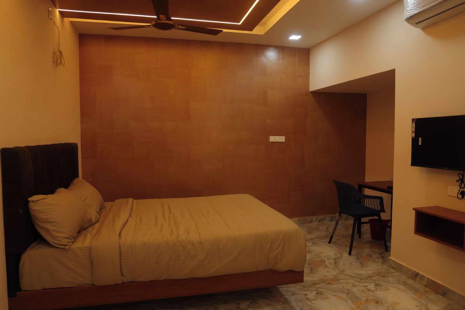 Un dormitorio con cama, escritorio, silla, televisor y ventilador de techo.