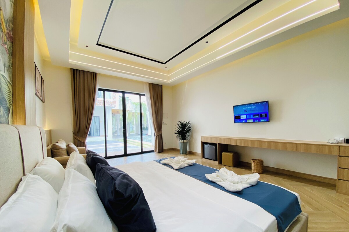 A modern hotel room with a large bed, a flat-screen TV, a desk, and a view of the outside.