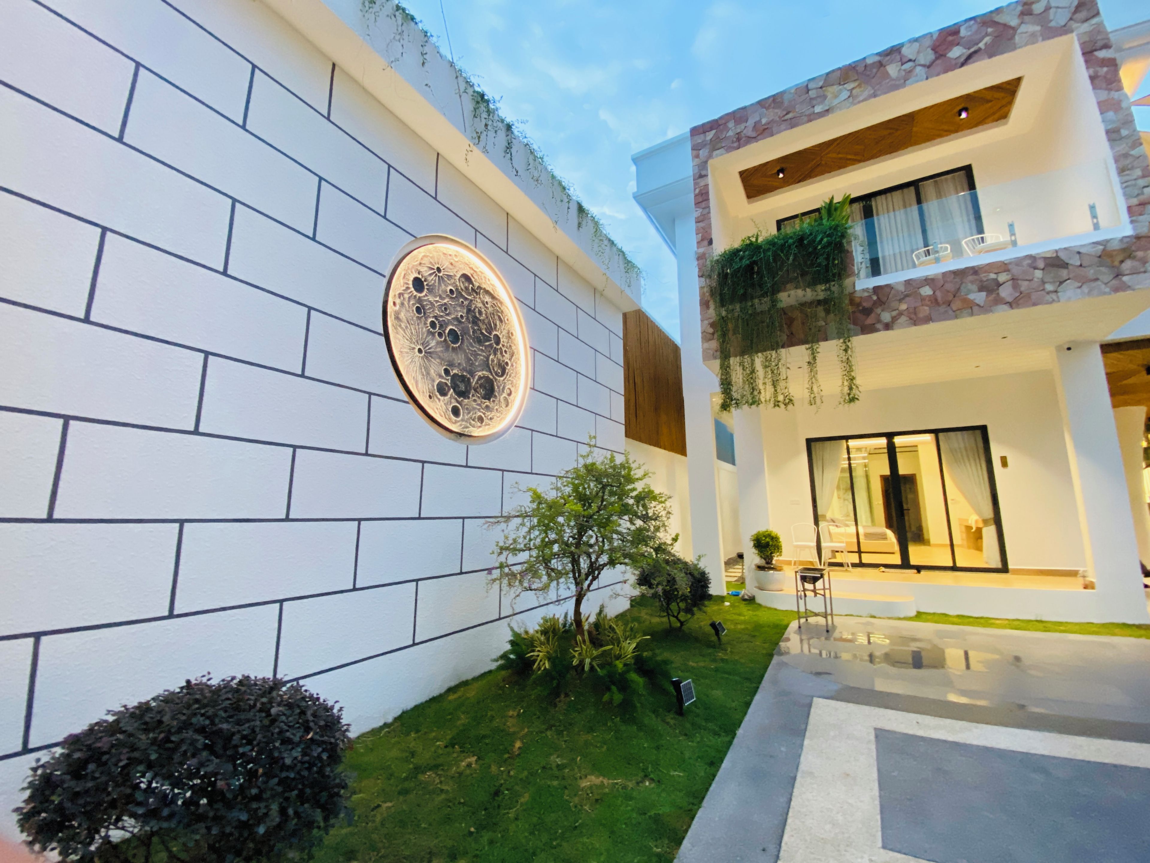 Un edificio moderno con fachada de ladrillo blanco, un elemento decorativo circular y un balcón con vegetación.