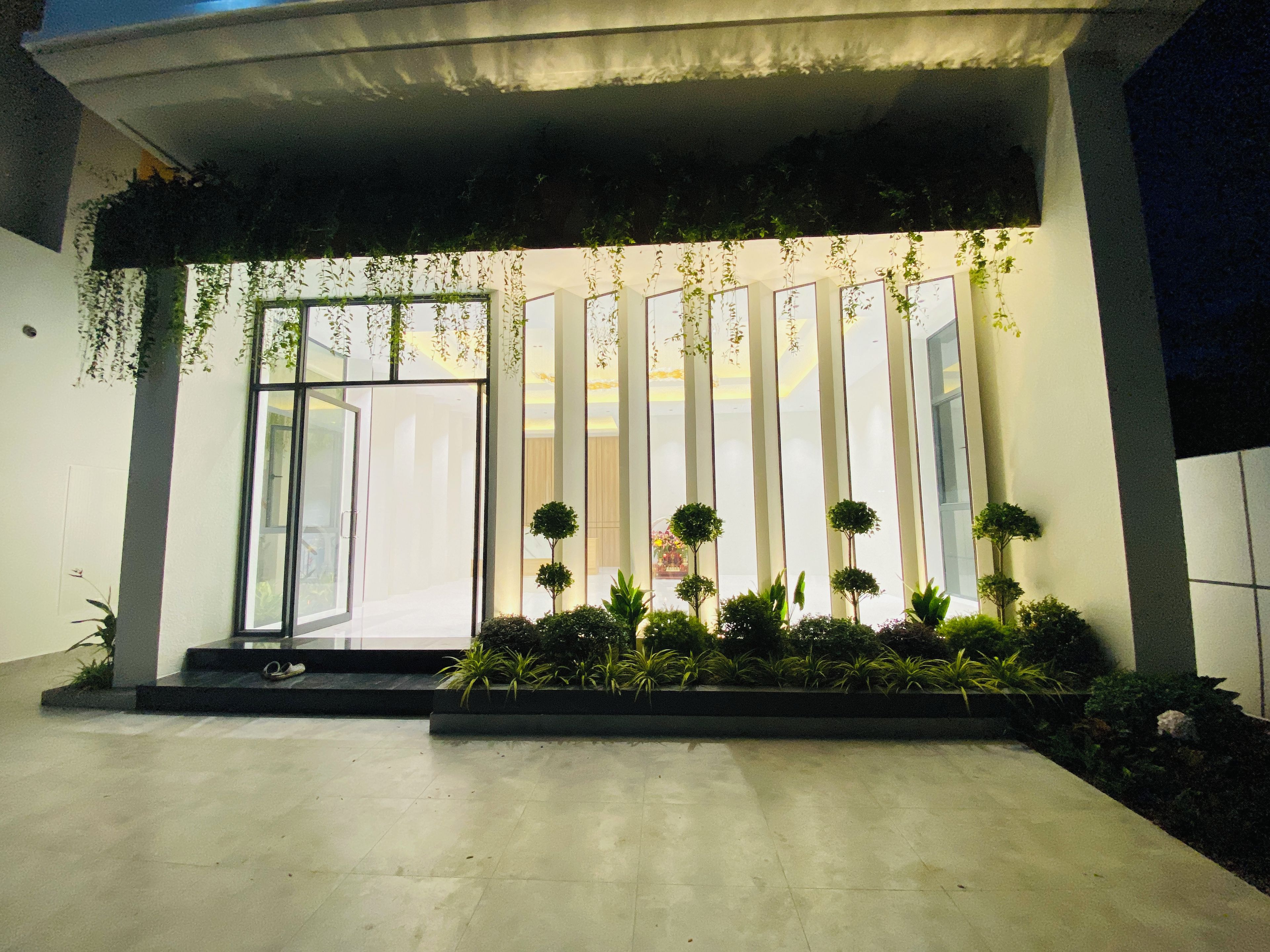 Una entrada moderna de edificio con puerta de vidrio, jardín vertical y plantas en macetas.