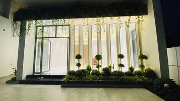 Una entrada moderna de edificio con puerta de vidrio, jardín vertical y plantas en macetas.