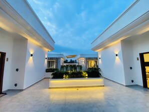 Un amplio patio con zona de estar central, rodeado de paredes blancas e iluminado con luz ambiental.