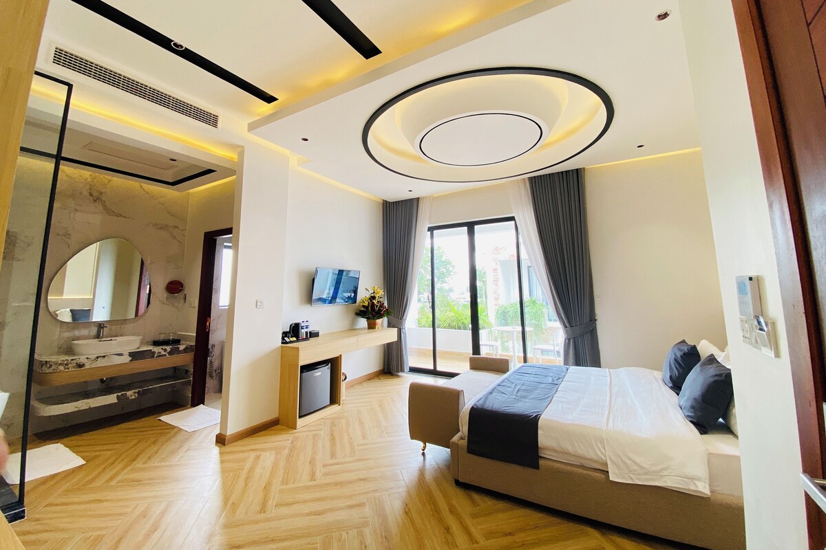 A modern hotel room with a large bed, a desk, a vanity with a mirror, and a view of the outdoors.