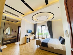 A modern hotel room with a large bed, a desk, a vanity with a mirror, and a view of the outdoors. - Kampot Hampton Villa (Kampot)