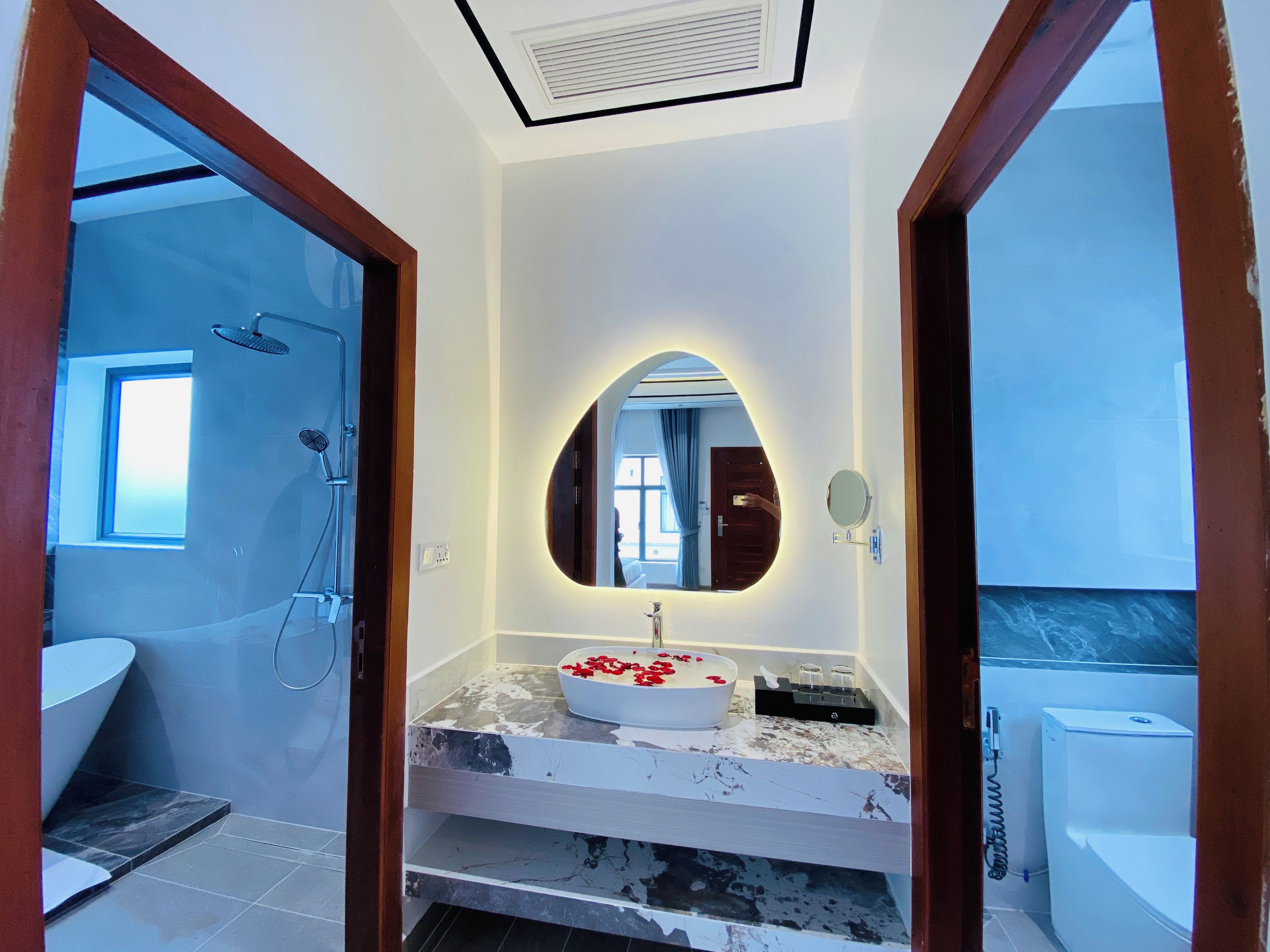 Une salle de bain moderne avec un grand miroir ovale, un lavabo blanc et une douche.