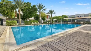Ein Swimmingpool mit Liegestühlen und Sonnenschirmen, umgeben von Bäumen und Gebäuden.