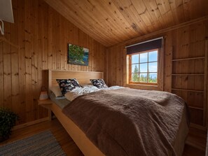 Ein Schlafzimmer mit Holzwänden, einem Bett, einem Nachttisch, einem Fenster mit Blick und einem Bild an der Wand.