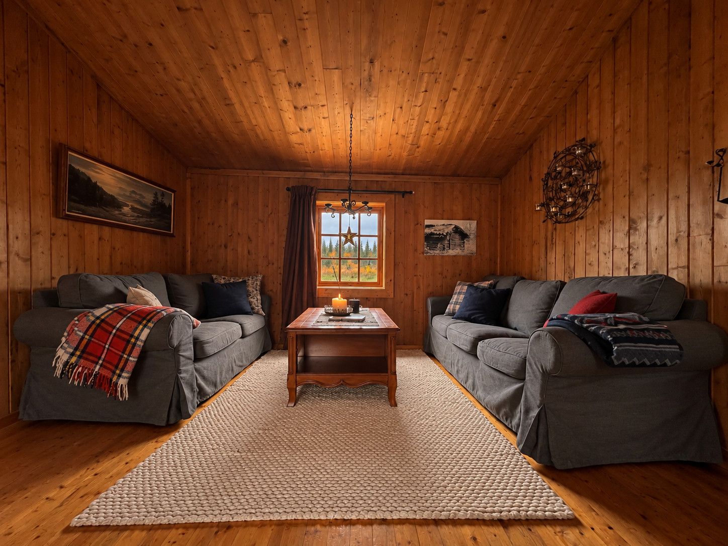 Quarto aconchegante estilo cabana com dois sofás cinzas, teto de madeira, tapete e janela com vista para árvores.