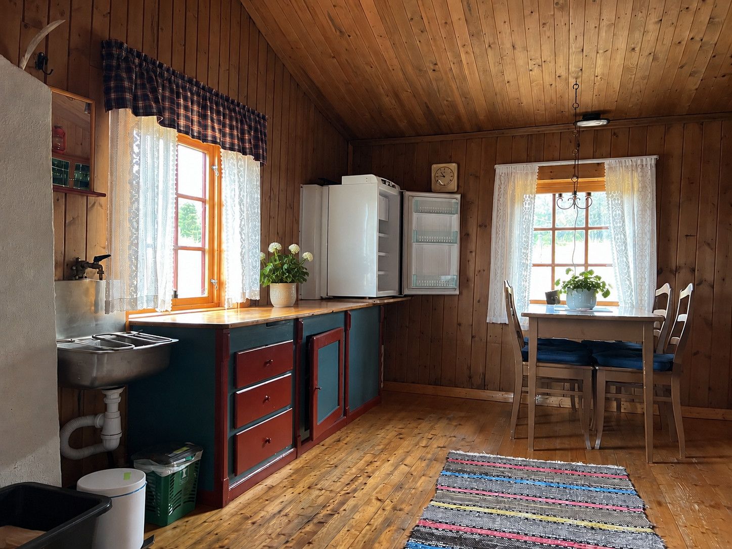 Interior de una cabaña de madera con cocina, que incluye un lavamanos, armarios y un refrigerador.