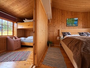 Habitación de cabaña de madera con literas, un escritorio, una cama con cabecera, una ventana y un cuadro en la pared.