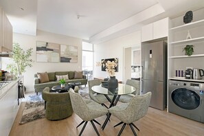 Una cocina moderna con lavadora integrada, un comedor con mesa y sillas de vidrio, y una sala de estar con sofá y mesa de centro.