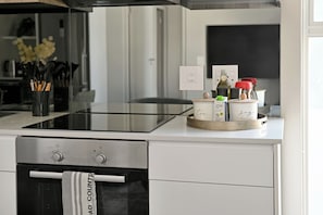 A modern kitchen with a stainless steel oven, a glass stovetop, and a countertop with kitchen utensils and containers. - Cape Town City 2-Bed, Views, Balcony & Pool (Cape Town)