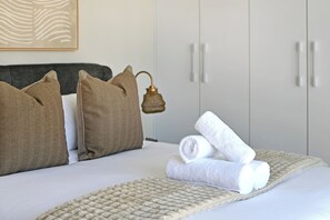 A neatly made bed with pillows, a rolled towel, and a textured blanket. - Cape Town City 2-Bed, Views, Balcony & Pool (Cape Town)