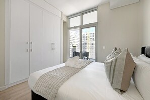 Una habitación de hotel con una cama grande, un ventanal con vistas a edificios y un armario.
