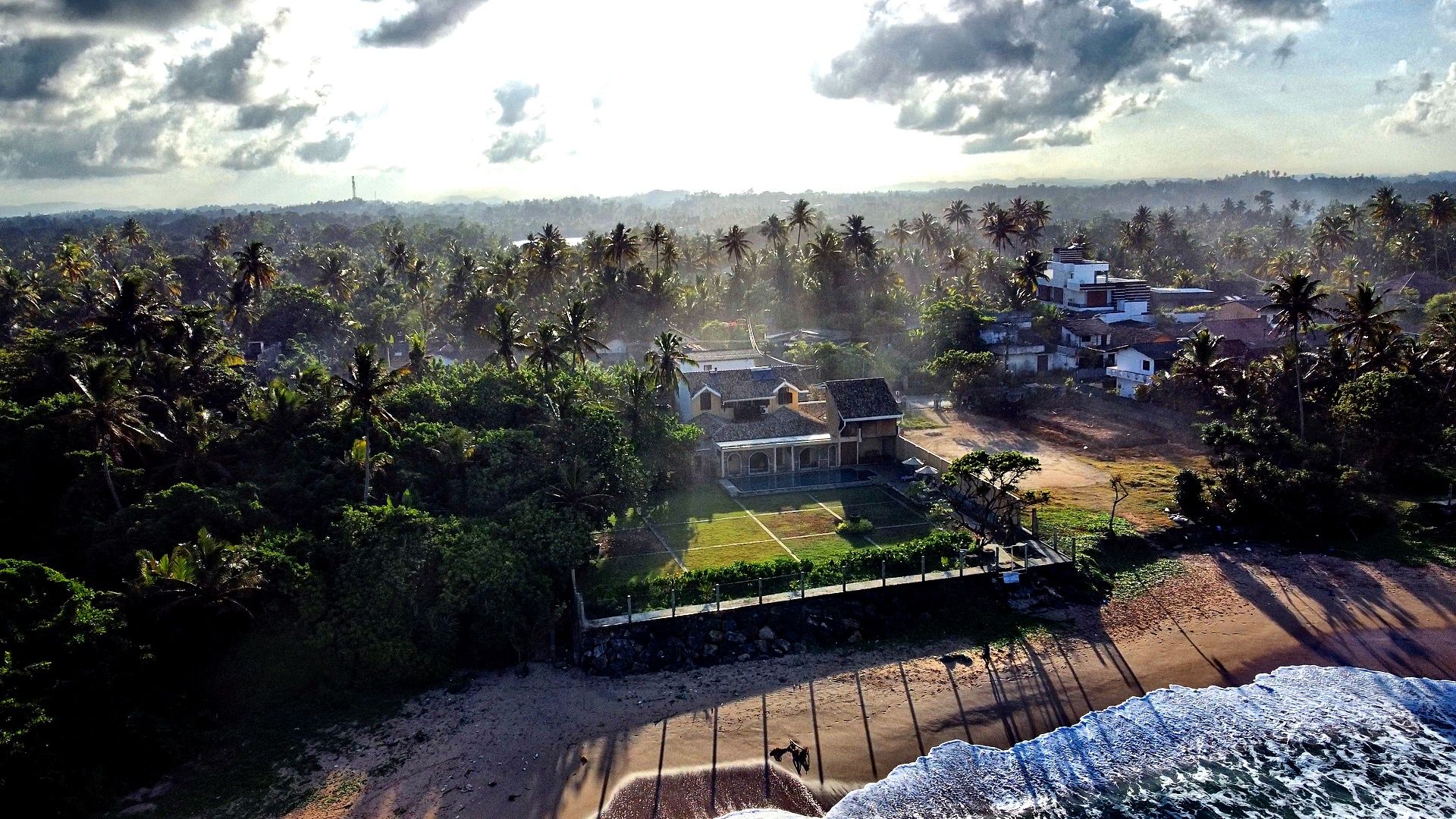 A coastal property with a large house, a tennis court, and a beach.
