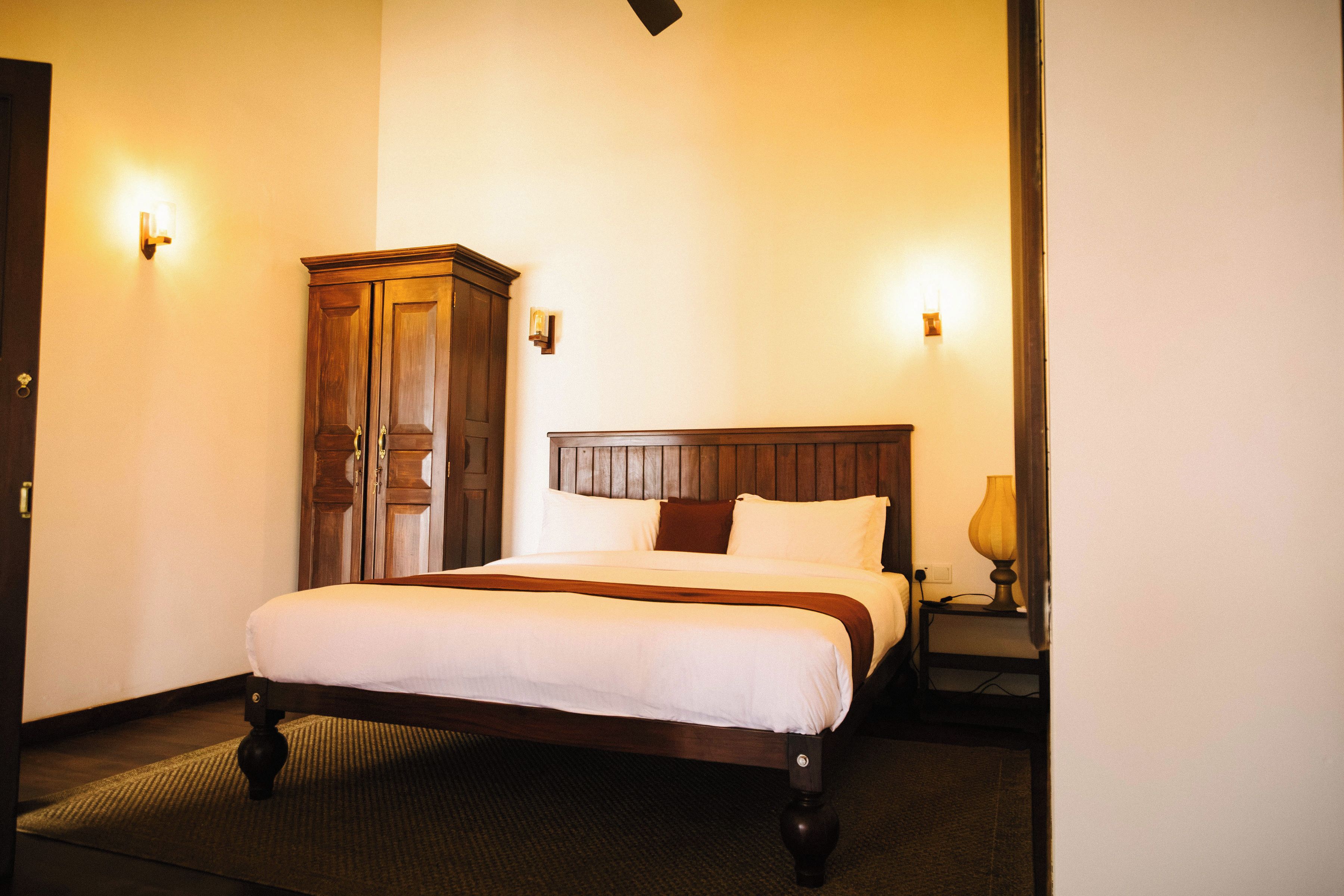 Une chambre d’hôtel avec un lit en bois, une armoire et deux lampes fixées au mur.