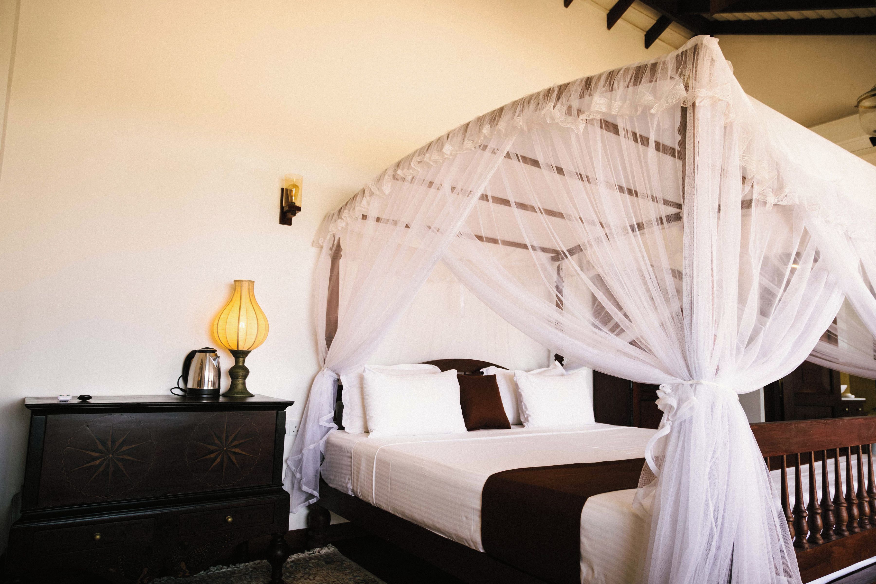 A four-poster bed with a canopy, a bedside table with a lamp, and a dresser.