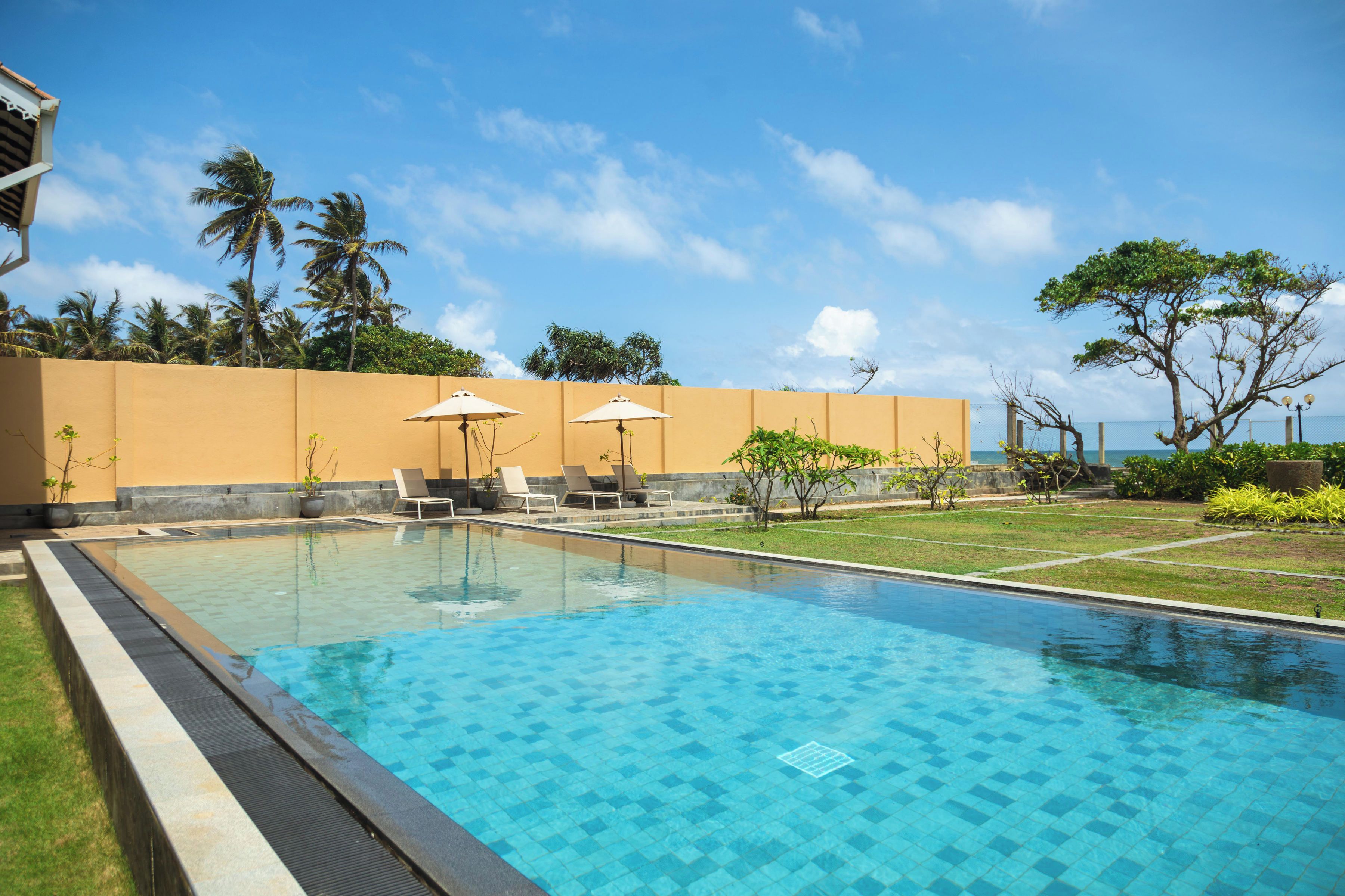 A swimming pool with lounge chairs and umbrellas, surrounded by palm trees and a clear sky.