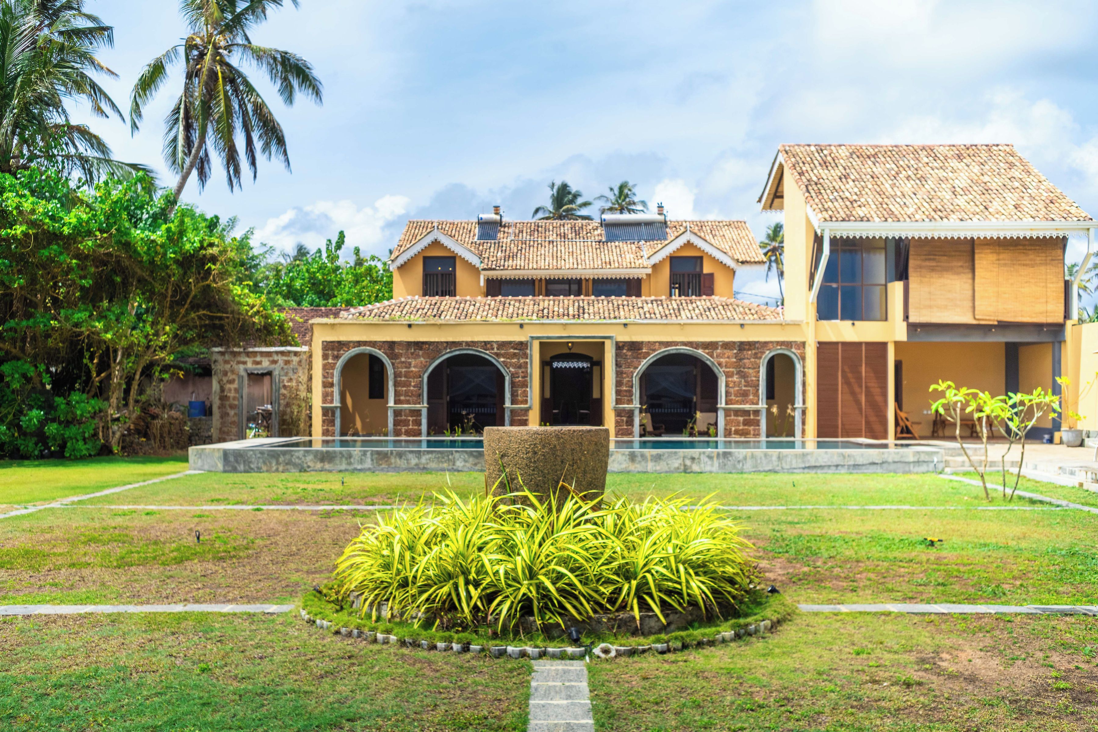 A two-story building with a tiled roof, a swimming pool, and a well-maintained garden with tropical plants.