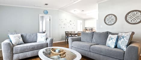 A modern living room with two grey sofas, a glass coffee table, wooden flooring, and a ceiling fan.