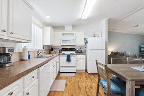 A compact kitchen with white cabinetry, a stove, microwave, and a refrigerator. - Chubby Mermaid! NEW!  Private Covered Dock & Saltwater Canal / Small Dogs ok. (Edgewater)