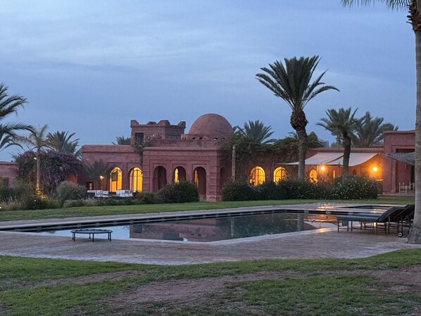 A courtyard with a pool, palm trees, and a building with arched windows and a dome.