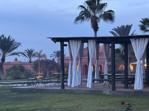 An outdoor seating area with tables and chairs, a covered pavilion, and palm trees. - Atlas-view estate with staff, 20m pool and tennis (Marrakesh)