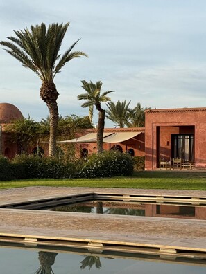 A pool with a reflection, palm trees, and a building with arches. - Atlas-view estate with staff, 20m pool and tennis (Marrakesh)