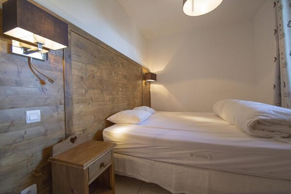 Ein Einzelbett mit weißer Bettwäsche, ein Nachttisch, eine Wandleuchte und ein Holz-Kopfteil.
