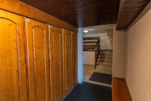 Ein Holzhäuschen mit einer Metalttür, einer Holztreppe und einem Metallgitter am unteren Rand.