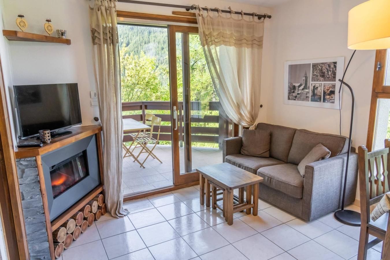 Un salon avec une cheminée, un canapé, un téléviseur et une vue sur un balcon aménagé avec du mobilier d’extérieur.