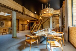 A spacious dining area with a high ceiling, wooden beams, and a chandelier. - Chalet, fitness, terrace, fireplace or stove, parking, tv, ski locker, 310m², Les 2 Alpes (Mont-de-Lans)