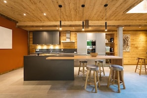 A modern kitchen with a central island, bar stools, and built-in appliances. - Chalet, fitness, terrace, fireplace or stove, parking, tv, ski locker, 310m², Les 2 Alpes (Mont-de-Lans)