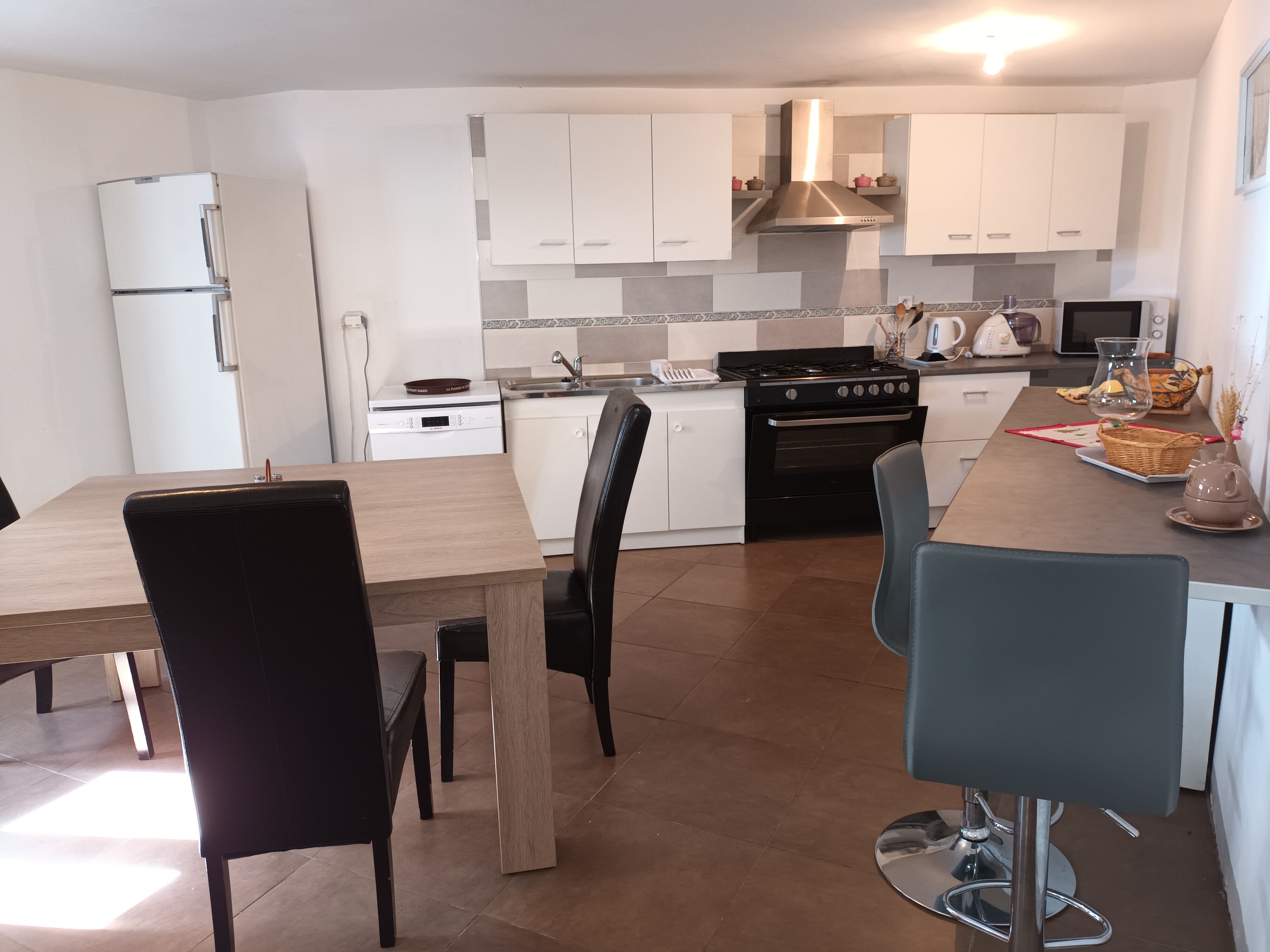 Une cuisine moderne avec des meubles blancs, une cuisinière noire et un coin repas comprenant une table en bois et des chaises noires.