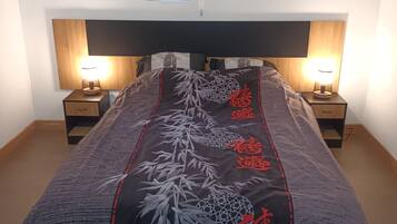 Un lit avec une couvre-lit à motifs, deux tables de chevet avec des lampes, un téléviseur fixé au mur et une petite fenêtre.