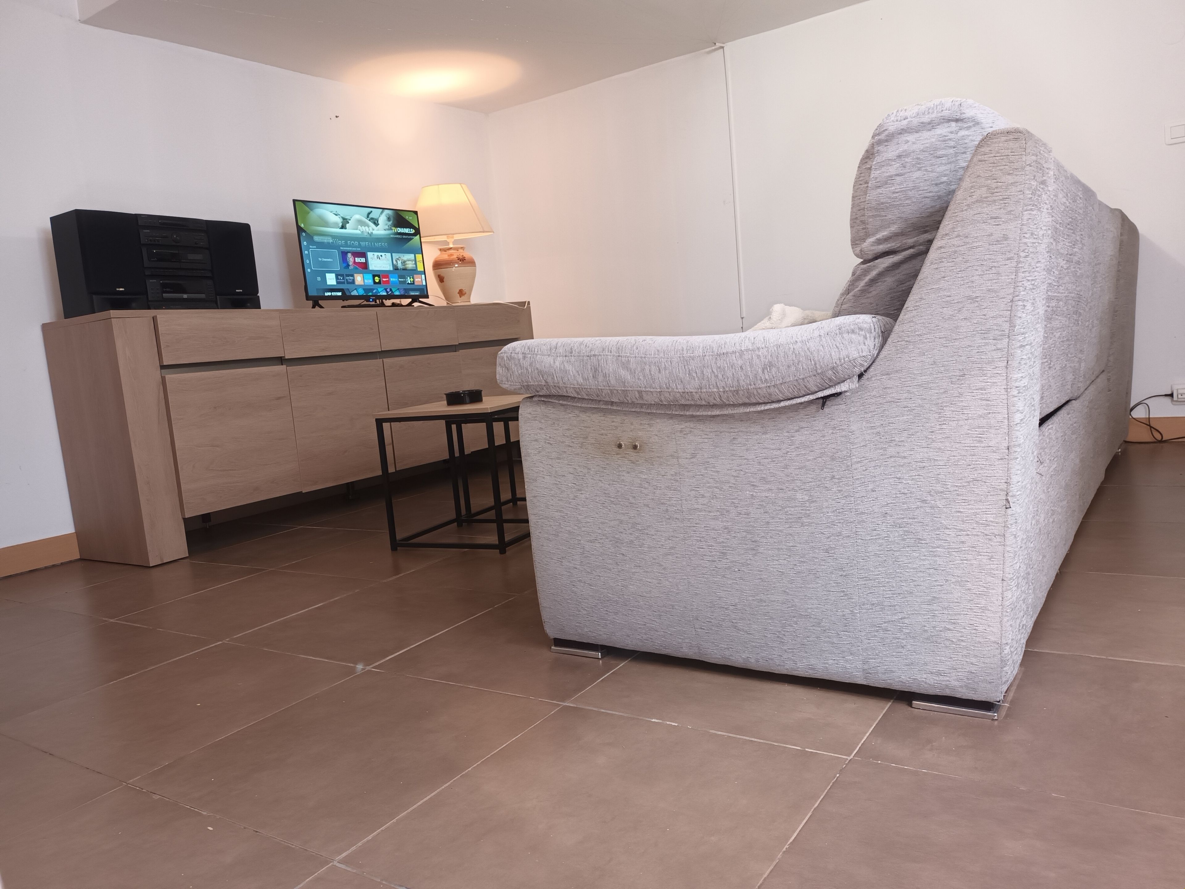 Un salon avec un fauteuil gris, un meuble en bois et un téléviseur à écran plat.