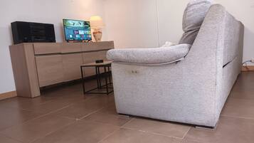 Un salon avec un fauteuil gris, un meuble en bois et un téléviseur à écran plat.