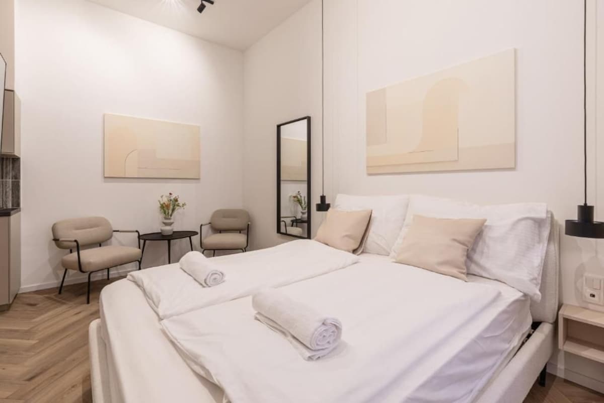 Ett hotellrum med en stor säng, två stolar, ett litet bord och konstverk på väggarna.