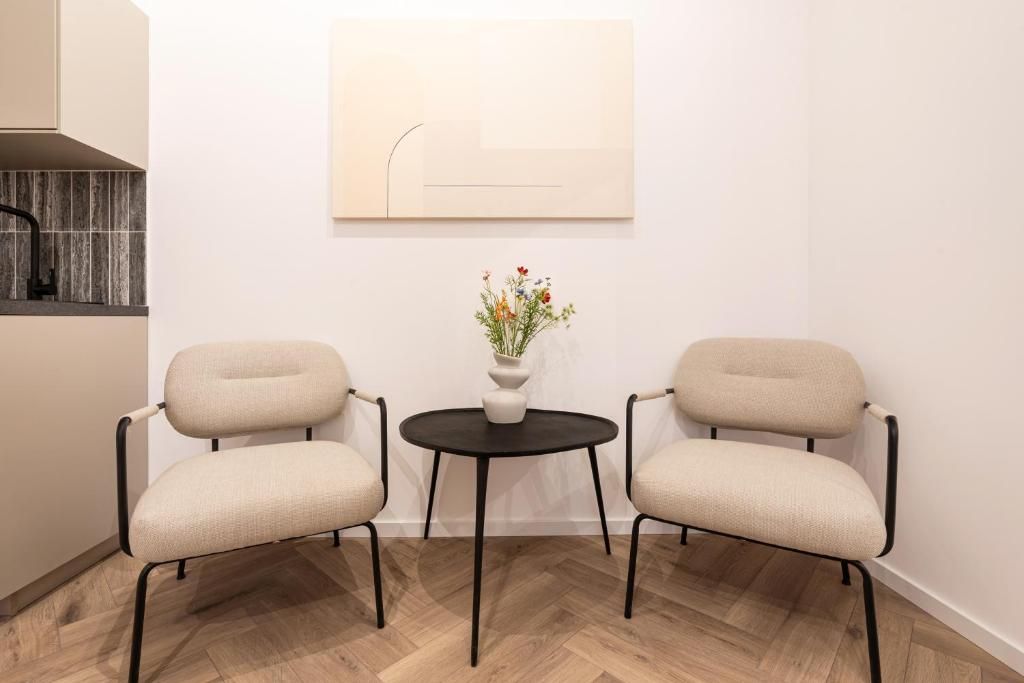 Een kamer met twee stoelen, een tafeltje met een bloevas en een kunstwerk aan de muur.