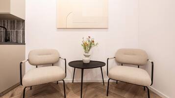 Een kamer met twee stoelen, een tafeltje met een bloevas en een kunstwerk aan de muur.