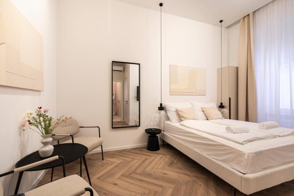 Een moderne slaapkamer met een bed, een fauteuil, een klein tafeltje, een spiegel en kunstwerken aan de wanden.