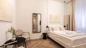Een moderne slaapkamer met een bed, een fauteuil, een klein tafeltje, een spiegel en kunstwerken aan de wanden.