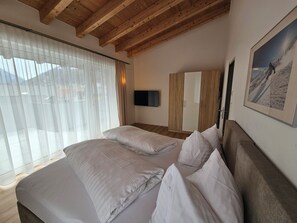 A bedroom with a large bed, a TV mounted on the wall, and a window with sheer curtains. - Deluxe Apartment in the Stubai Valley—where high standards meet cozy comfort (Fulpmes)