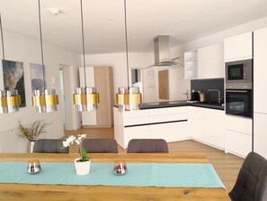 A modern kitchen with white cabinets, a microwave, and an oven. There is a dining area with a wooden table and chairs, and a vase with flowers. - Deluxe Apartment in the Stubai Valley—where high standards meet cozy comfort (Fulpmes)