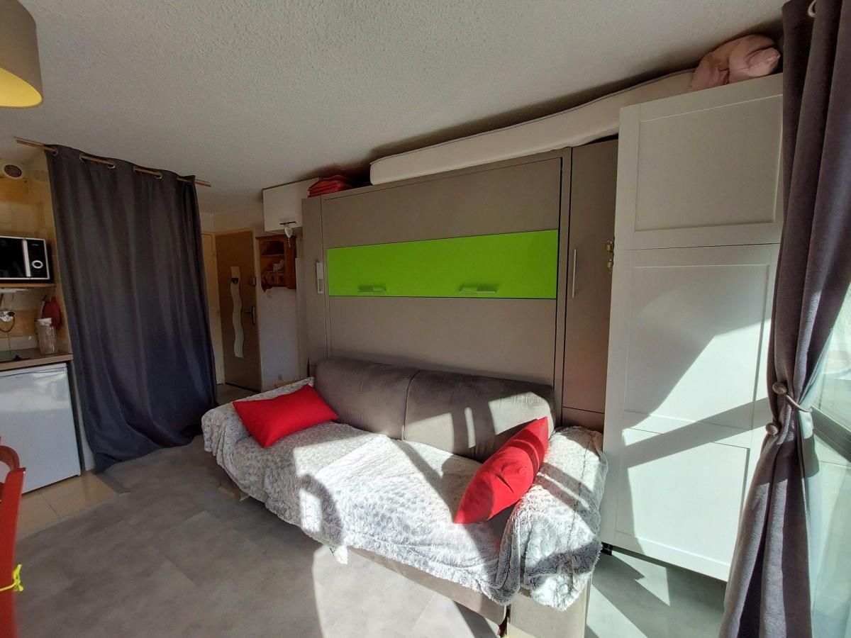 A compact room with a bed, a small desk, a wardrobe, and a window with curtains.