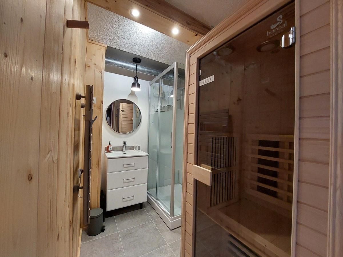 A wooden interior with a sauna, a glass-enclosed shower, and a white vanity with a mirror.